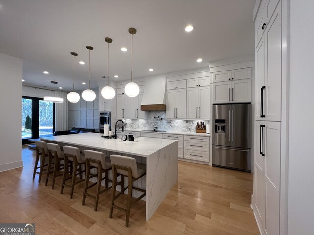 kitchen with appliances with stainless steel finishes, custom range hood, hanging light fixtures, light stone countertops, and white cabinets