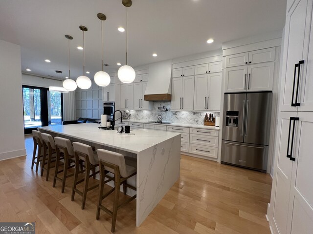 kitchen featuring white cabinets, stainless steel appliances, a large island, light stone counters, and custom range hood