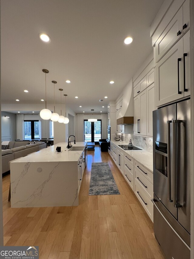 kitchen with a large island with sink, white cabinets, high end refrigerator, and custom range hood