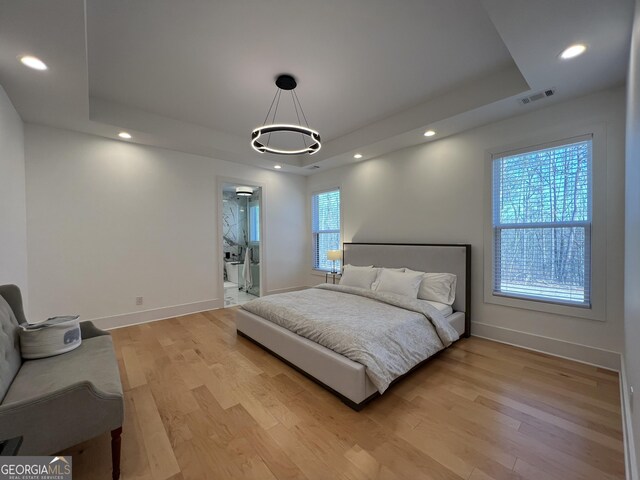 bedroom with light hardwood / wood-style floors, a tray ceiling, and ensuite bath