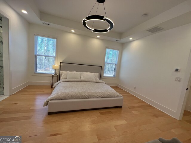 bedroom with light wood-type flooring, a tray ceiling, and multiple windows