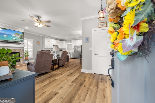 foyer with ceiling fan, light wood-type flooring, a fireplace, and crown molding