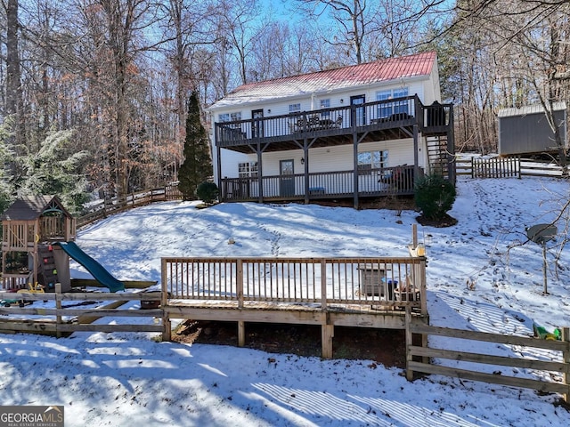 snow covered property with a deck and a playground