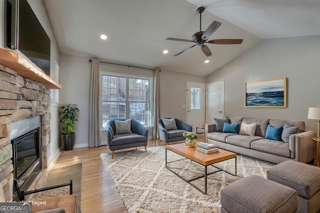 living room with lofted ceiling, a stone fireplace, ceiling fan, and light wood-type flooring