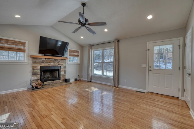 unfurnished living room with ceiling fan, a stone fireplace, a wealth of natural light, and light wood-type flooring