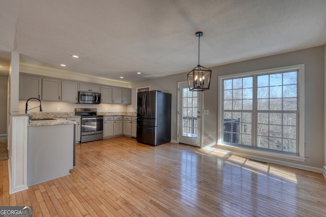 kitchen featuring appliances with stainless steel finishes, sink, hanging light fixtures, a notable chandelier, and light wood-type flooring