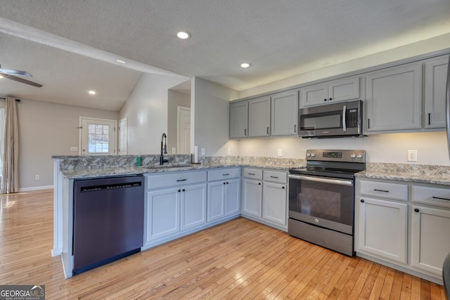 kitchen with vaulted ceiling, appliances with stainless steel finishes, sink, ceiling fan, and light hardwood / wood-style floors