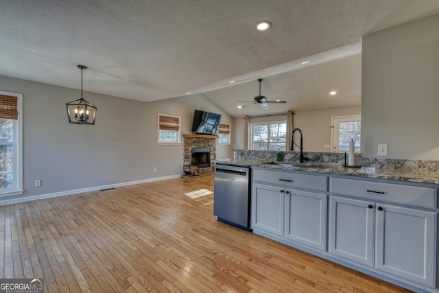 kitchen with a stone fireplace, sink, stainless steel dishwasher, ceiling fan, and a textured ceiling