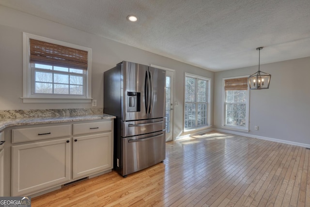 kitchen featuring light stone counters, a textured ceiling, light wood-type flooring, stainless steel fridge, and white cabinets