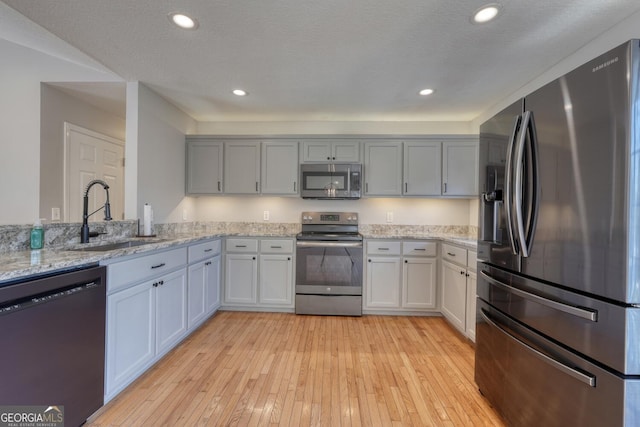 kitchen featuring sink, light stone counters, a textured ceiling, light wood-type flooring, and stainless steel appliances