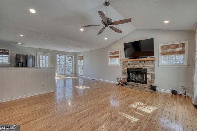 unfurnished living room featuring a stone fireplace, vaulted ceiling, ceiling fan, and light wood-type flooring