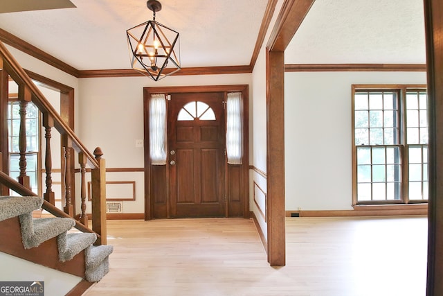 foyer entrance with crown molding, a chandelier, and light hardwood / wood-style flooring