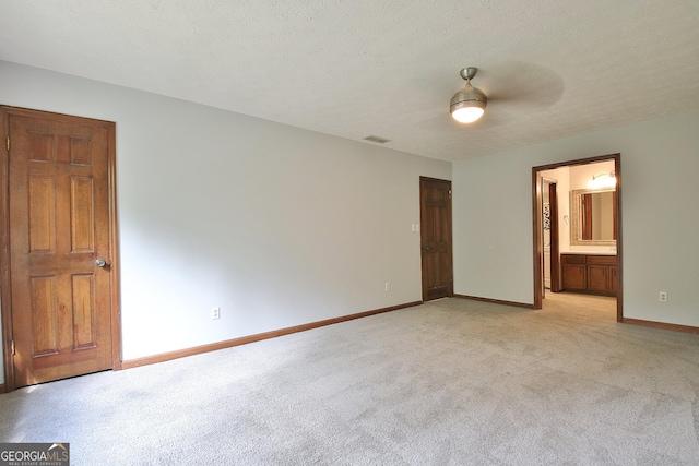 unfurnished bedroom featuring ceiling fan, a textured ceiling, ensuite bathroom, and light carpet