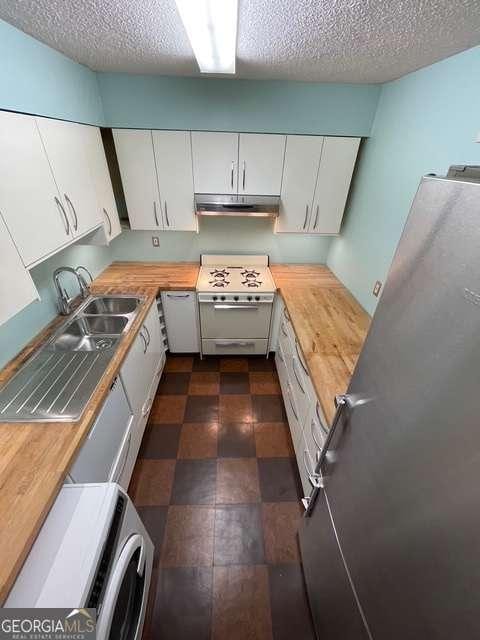 kitchen with stainless steel fridge, white cabinets, range, and a textured ceiling