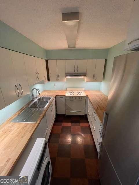 kitchen with wooden counters, washer / clothes dryer, sink, stainless steel refrigerator, and stove