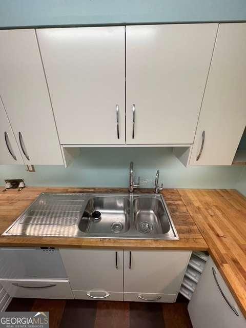 room details featuring sink, white cabinetry, and wood counters