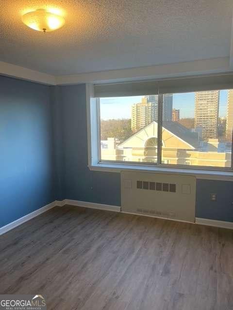 unfurnished room with wood-type flooring, radiator heating unit, and a textured ceiling