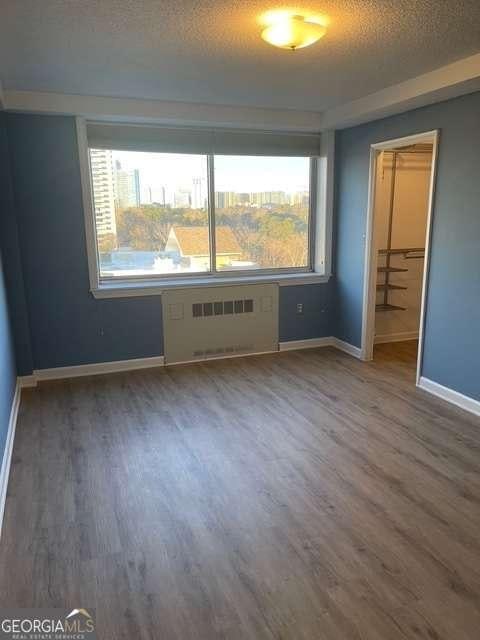 unfurnished bedroom featuring a spacious closet, a closet, wood-type flooring, a textured ceiling, and radiator heating unit