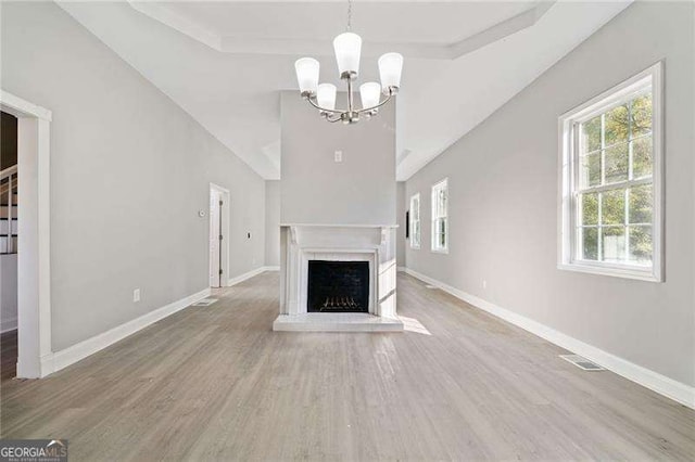 unfurnished living room with hardwood / wood-style flooring, a tray ceiling, an inviting chandelier, and a fireplace