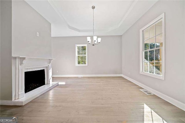 unfurnished living room featuring light hardwood / wood-style flooring, a raised ceiling, and a notable chandelier