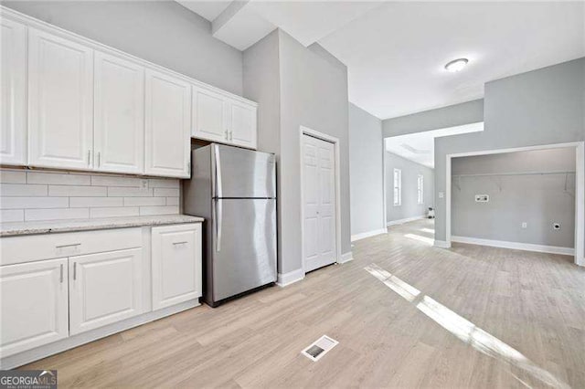 kitchen featuring light wood-type flooring, backsplash, stainless steel fridge, and white cabinetry