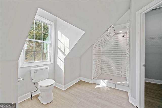 bathroom featuring toilet, a tile shower, and vaulted ceiling