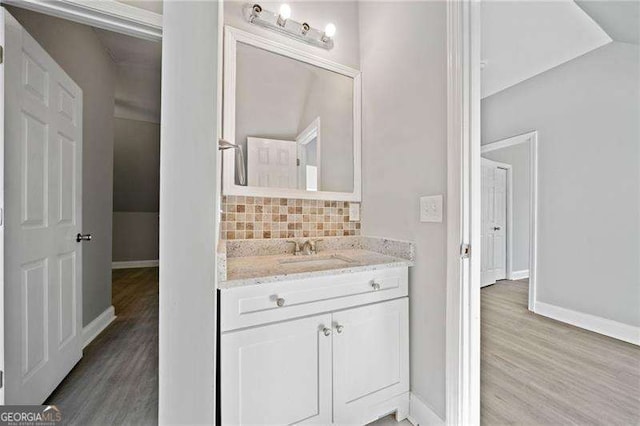 bathroom featuring lofted ceiling, vanity, backsplash, and wood-type flooring