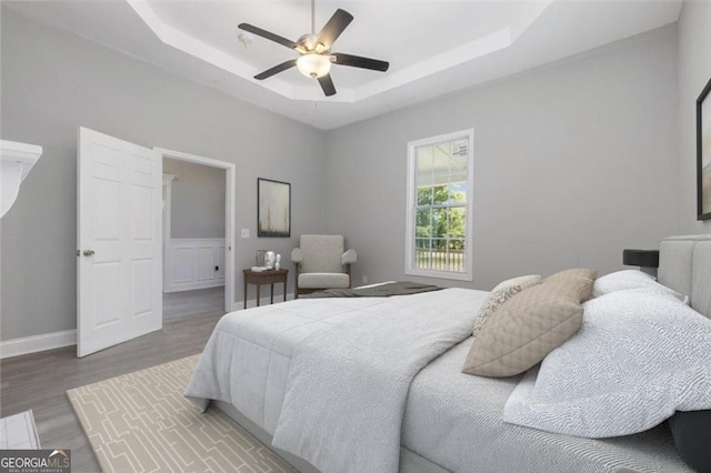 bedroom with ceiling fan, wood-type flooring, and a raised ceiling