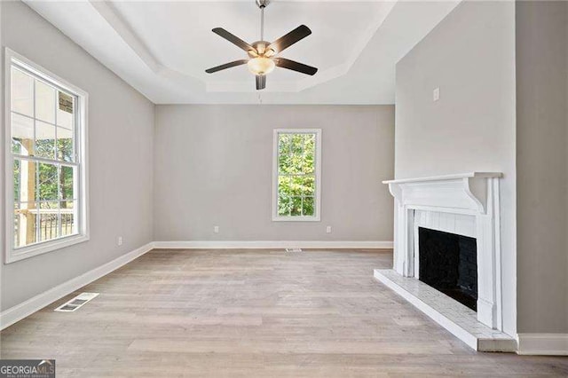 unfurnished living room featuring ceiling fan, light hardwood / wood-style floors, and a raised ceiling