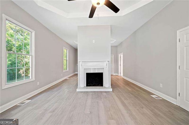 unfurnished living room with a raised ceiling, ceiling fan, a brick fireplace, and light hardwood / wood-style floors