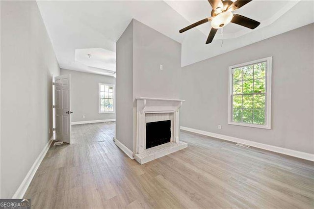 unfurnished living room featuring ceiling fan, plenty of natural light, a tray ceiling, and light hardwood / wood-style floors