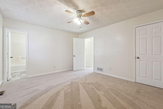 unfurnished bedroom with light carpet, ceiling fan, ensuite bathroom, and a textured ceiling