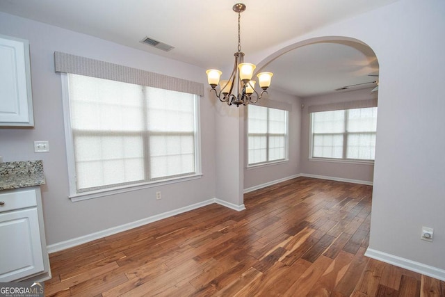 unfurnished dining area featuring dark hardwood / wood-style flooring and ceiling fan with notable chandelier