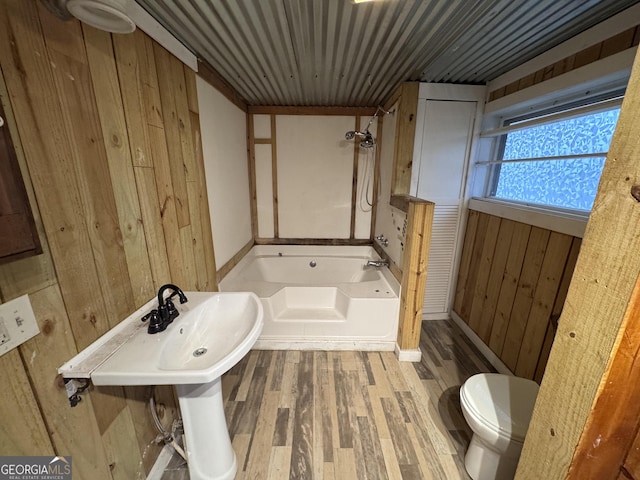 bathroom with toilet, a tub to relax in, hardwood / wood-style flooring, and wooden walls