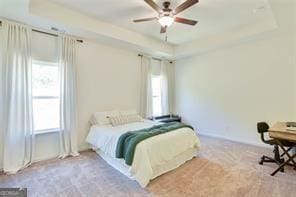 carpeted bedroom with ceiling fan and a raised ceiling