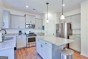 kitchen with appliances with stainless steel finishes, a center island, decorative light fixtures, light stone counters, and sink