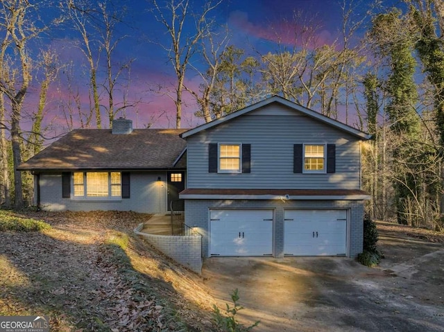 split level home featuring driveway, brick siding, a chimney, and an attached garage