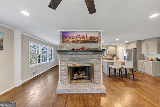 living area with dark wood-type flooring, a brick fireplace, crown molding, and baseboards