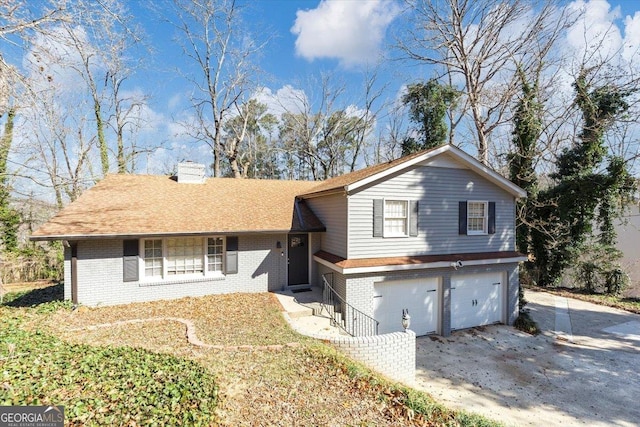 split level home featuring a garage, driveway, a chimney, roof with shingles, and brick siding