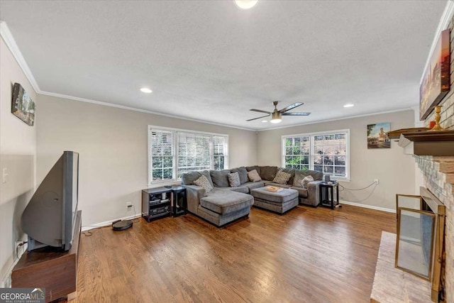 living area with baseboards, ornamental molding, wood finished floors, and a stone fireplace