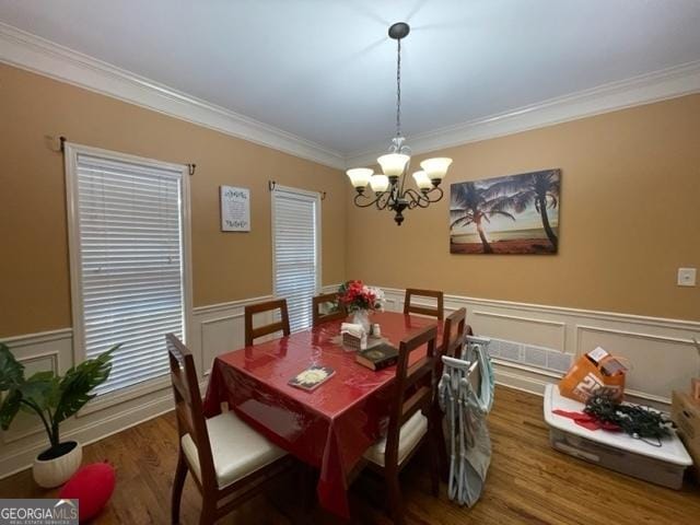 dining area featuring dark wood-type flooring, ornamental molding, and an inviting chandelier