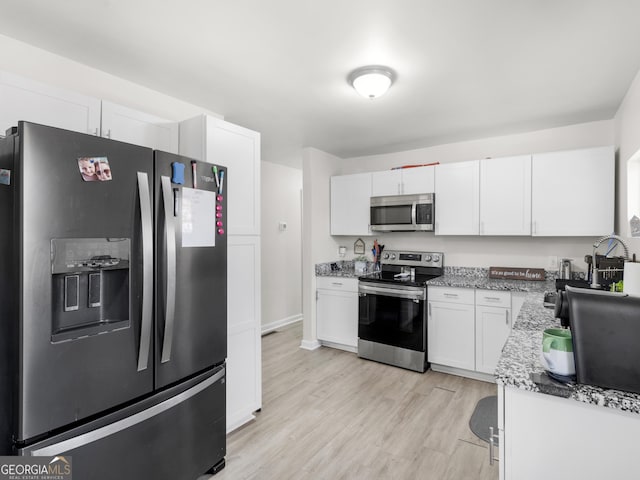 kitchen with light stone counters, stainless steel appliances, white cabinets, and light wood-type flooring