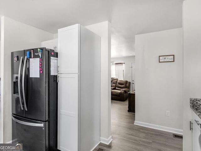 kitchen with white cabinetry, stone countertops, fridge with ice dispenser, and hardwood / wood-style flooring