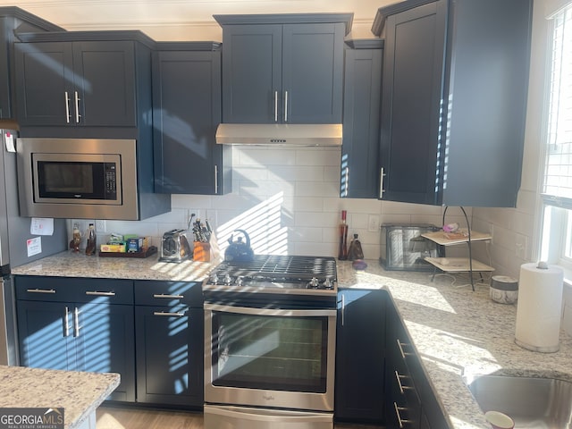 kitchen featuring light stone countertops, backsplash, stainless steel appliances, and blue cabinets