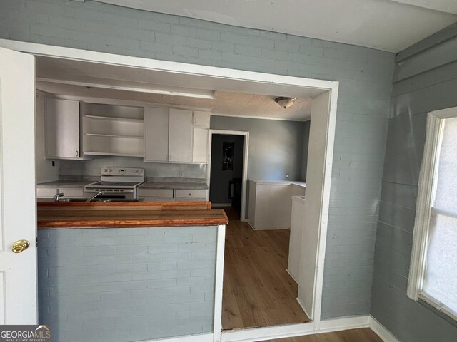 kitchen with butcher block countertops, electric stove, white cabinetry, and light hardwood / wood-style flooring