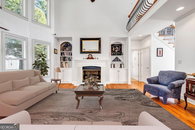 living area featuring a fireplace with flush hearth, wood finished floors, baseboards, stairs, and built in features