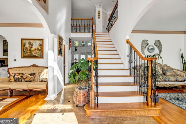 staircase with decorative columns, a high ceiling, crown molding, and wood finished floors