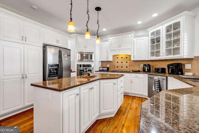 kitchen with white cabinets, a kitchen island, glass insert cabinets, stainless steel appliances, and light wood-type flooring