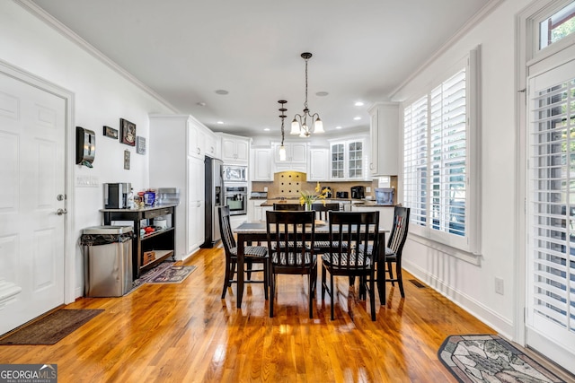 dining space with visible vents, light wood-type flooring, a wealth of natural light, and crown molding