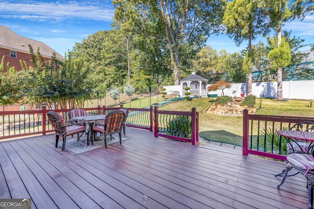 deck featuring outdoor dining space, a fenced backyard, a lawn, and a gazebo